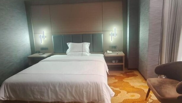 A hotel room with a bed, nightstands, a chair, and a headboard with built-in lighting.
