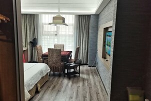 Habitación de hotel con cama, una mesa de comedor con sillas, ventilador de techo y un ventanal con cortinas.