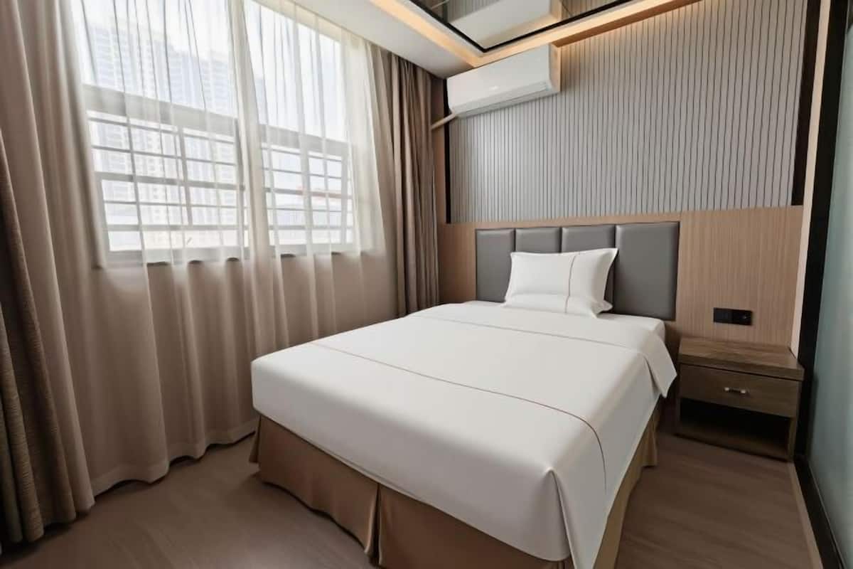 Una habitación de hotel moderna con una cama grande, una mesita de noche, un aire acondicionado de pared y una ventana con cortinas.