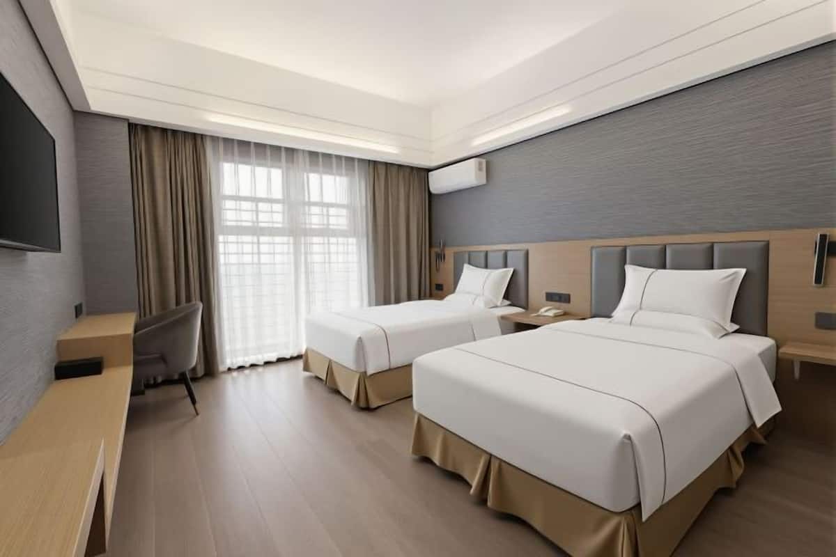 Habitación de hotel con dos camas, un escritorio, una silla y un televisor.
