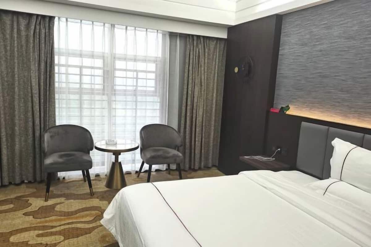 Habitación de hotel con cama, dos sillones, una mesita, un reloj de pared y ventana con cortinas.