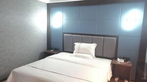 A hotel room with a bed, a nightstand, a phone, and a wall-mounted light fixture.