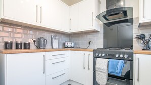 A modern kitchen with white cabinets, a stainless steel range hood, a built-in oven, and a coffee maker.