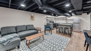 Een modern appartement met een grijze bank, een houten salontafel en een keukenhoek met een eettafel en barstoelen.