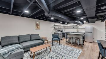 Un appartement moderne avec un canapé gris, une table basse en bois et un coin cuisine comprenant une table à manger et des tabourets de bar.