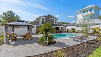 A backyard with a swimming pool, patio furniture, and a covered seating area.