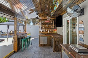 A bar area with wooden bar counter, stools, and a fan. - Stylish Panama City Home w/ Pool, Tiki Bar, & Walkable Beach Access (Panama City Beach)
