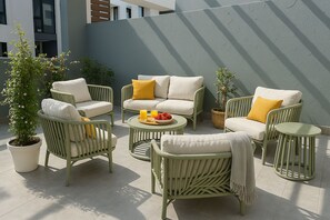 Espaço ao ar livre com mobiliário de vime, almofadas e uma mesa com frutas e bebidas.