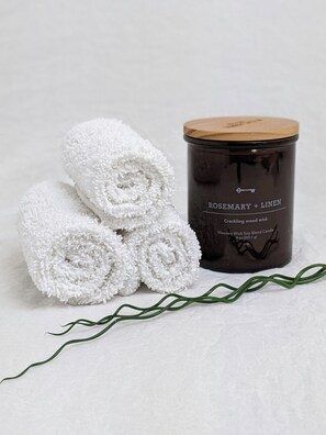 A candle labeled "ROSEMARY + LINEN" and rolled white towels. - Family & Friends HUGE House Dubai MALL Fast Ride (Dubai)