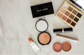 A makeup palette, a compact powder, a lipstick, a mascara, and a skincare product on a marble surface.