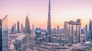 A cityscape with modern skyscrapers, including a prominent tower, and a complex network of roads. - Family & Friends HUGE House Dubai MALL Fast Ride (Dubai)