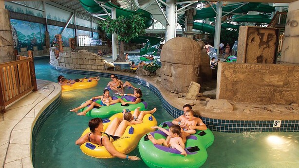 An indoor water park with multiple water slides, a large rock formation, and people on inflatable tubes. - NFL Draft or Easter week condo with indoor waterpark (Wisconsin Dells)