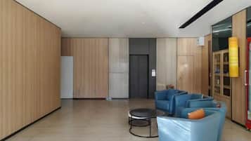 A modern lobby with a seating area, a reception desk, and a door leading to elevators.