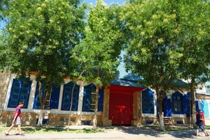 Un edificio con puerta roja y ventanas azules, rodeado de árboles.