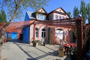 Ein traditionelles Gebäude mit roter und blauer Fassade, einer überdachten Veranda mit Sitzgelegenheiten und einer Treppe zum Eingang.