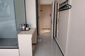 Pasillo de hotel con mostrador de recepción, perchero y puerta que da a otra habitación.