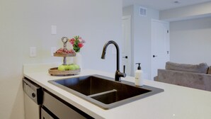 A modern kitchen with a double sink, a wooden fruit and flower display, and a bottle of hand soap. - The Gameday Landing at Stadium Place (Manhattan)