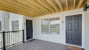 A covered porch with a wooden ceiling, a black door, and a large window. - The Gameday Landing at Stadium Place (Manhattan)