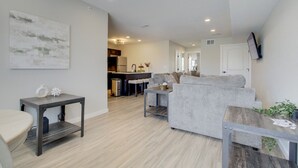 A modern living room with a grey sofa, a small table, and a kitchen in the background. - The Gameday Landing at Stadium Place (Manhattan)