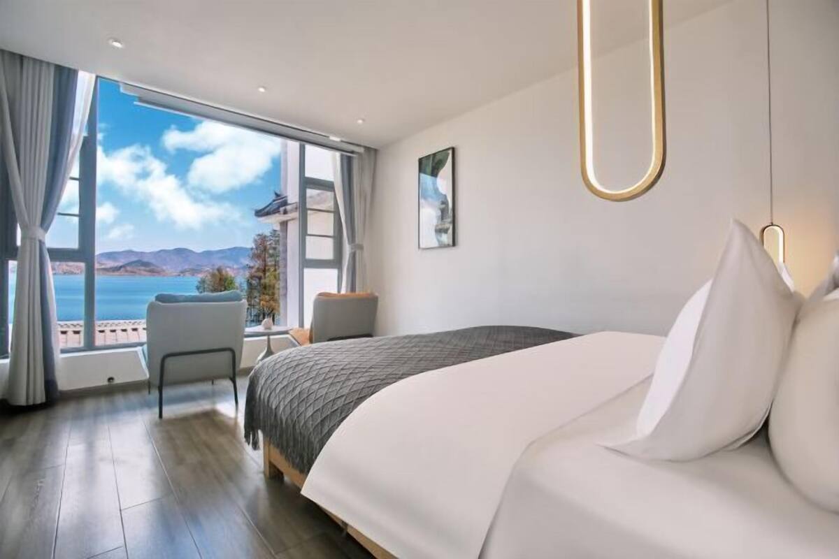 Quarto de hotel moderno com uma cama grande, área de estar e varanda com vista para o mar.