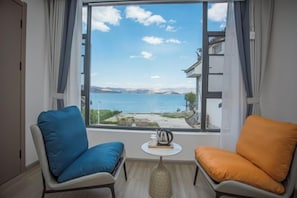 A room with two chairs facing a window overlooking a body of water and distant mountains. - Longkan Yunding Courtyard Hotel (Dali City)