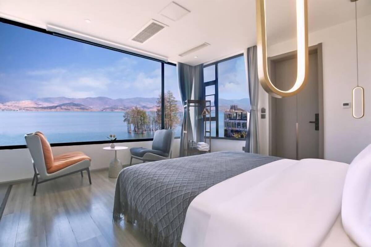 Quarto de hotel moderno com uma janela ampla, uma cama, uma cadeira e uma pequena mesa.