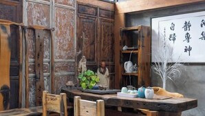 A rustic interior with wooden furniture, a traditional tea set, and a wall with calligraphy. - Longkan Yunding Courtyard Hotel (Dali City)
