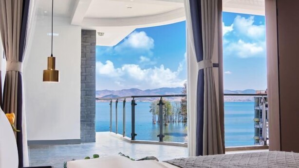 A bedroom with a large bed, a view of the sea, and a balcony with a railing. - Longkan Yunding Courtyard Hotel (Dali City)