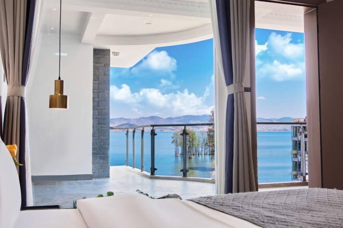 Quarto com uma cama grande, vista para o mar e varanda com guarda-corrimão.