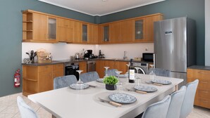 A modern kitchen with wooden cabinets, a stainless steel refrigerator, and a dining area set for six with placemats and plates.