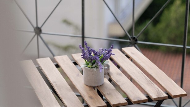 A wooden table with a potted plant on a balcony with a metal railing.