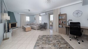 A spacious living room with a fireplace, a sofa, a coffee table, a bookshelf, a desk, and a modern chandelier.