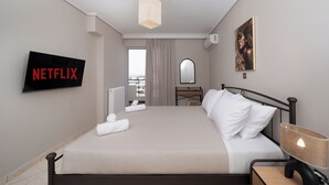 A hotel room with a bed, a TV mounted on the wall, a desk with a chair, a lamp, and a painting on the wall.