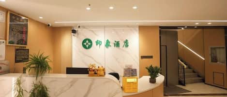 A hotel reception area with a marble counter, a green logo, and a staircase in the background.