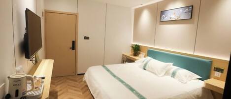 A hotel room with a bed, a desk with a computer, a TV, and a wall-mounted artwork.