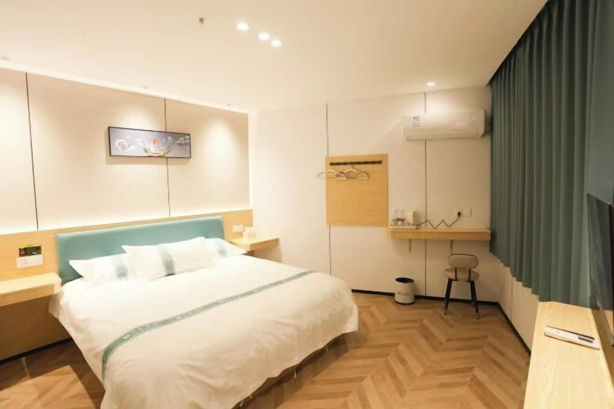 Quarto de hotel com uma cama, uma escrivaninha, uma cadeira, um espelho e uma televisão presa à parede.