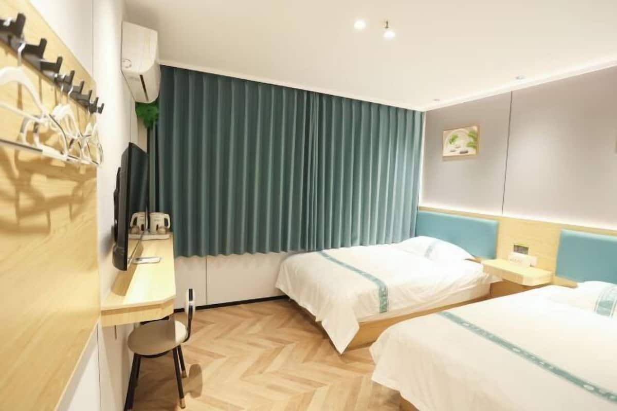 Quarto de hotel com duas camas, uma escrivaninha, uma cadeira, uma televisão e uma janela com cortinas.