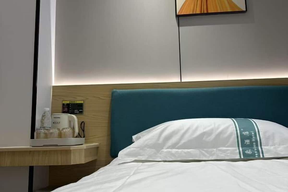 Quarto de hotel com uma cama, uma mesa de cabeceira com cafeteira e um painel de controle fixado na parede.