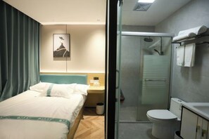 Habitación de hotel con cama, mesita de noche, cuadro enmarcado, ducha y retrete.