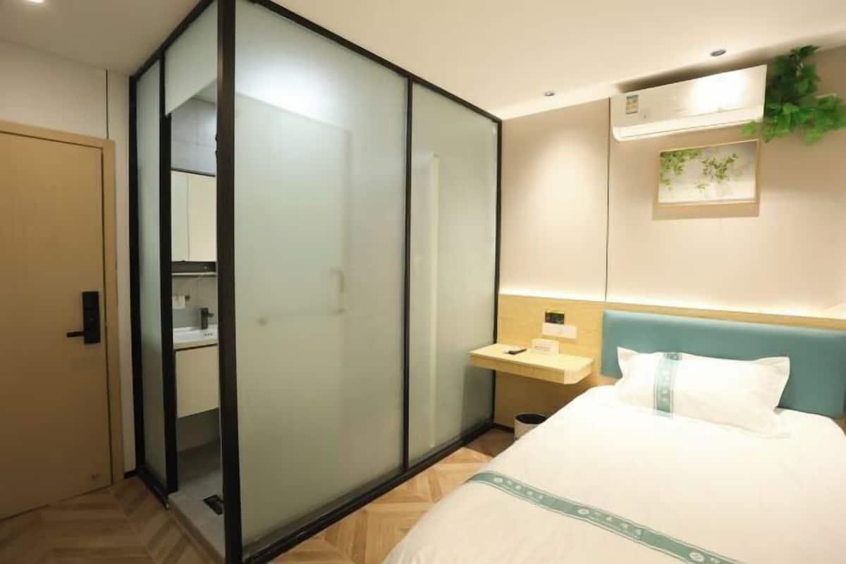 Quarto de hotel com cama, escrivaninha, guarda-roupa com portas de vidro jateado e ar condicionado fixado na parede.