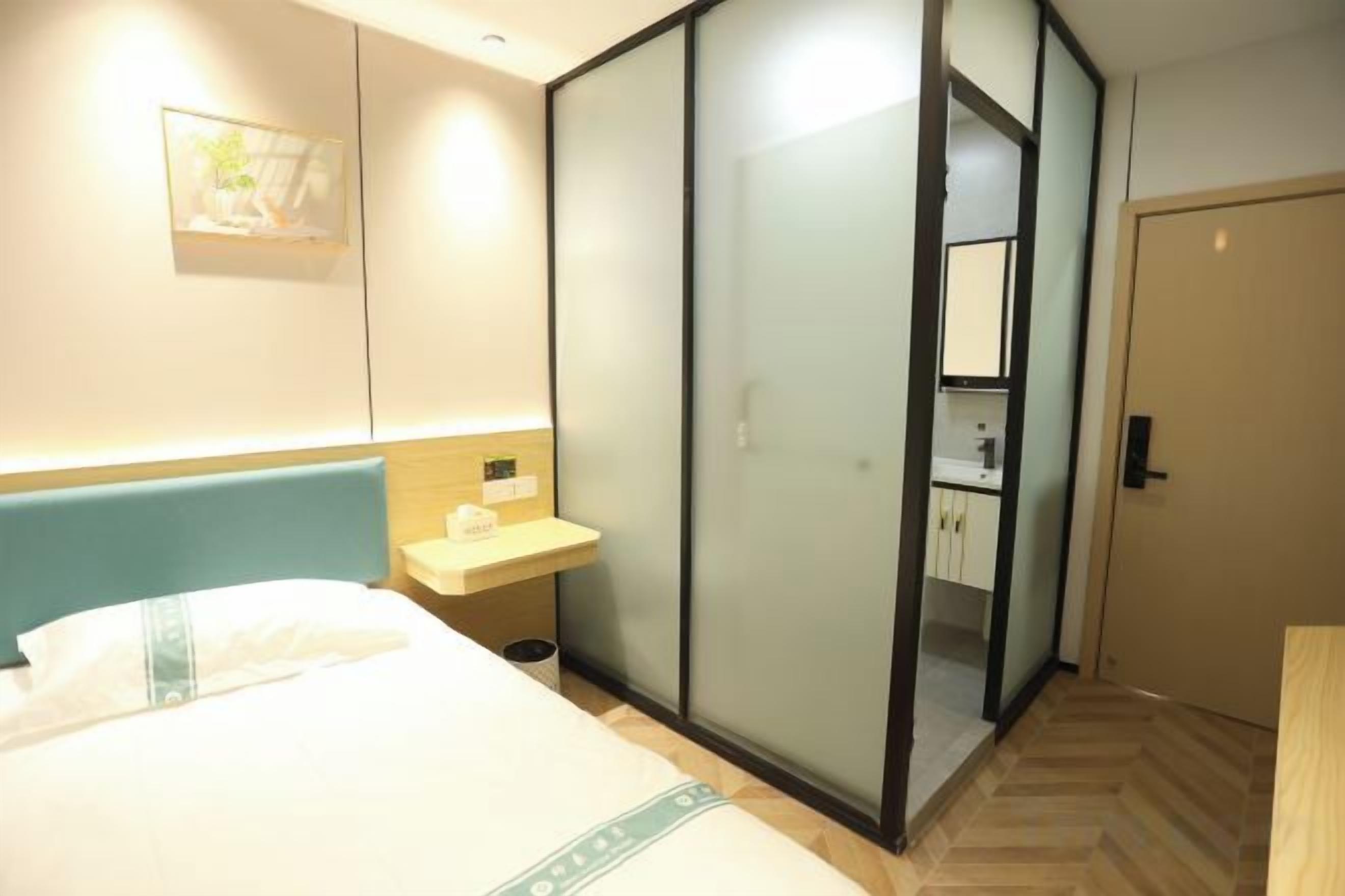 A hotel room with a bed, a bedside table, a sliding door closet, and a bathroom visible through the door.