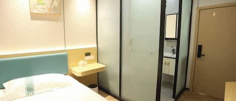 A hotel room with a bed, a bedside table, a sliding door closet, and a bathroom visible through the door.