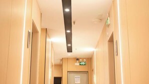 A hotel corridor with beige walls, a ceiling with recessed lighting, and an emergency exit sign above a door. - Shanghai Xinnuo Hotel (Shanghai)