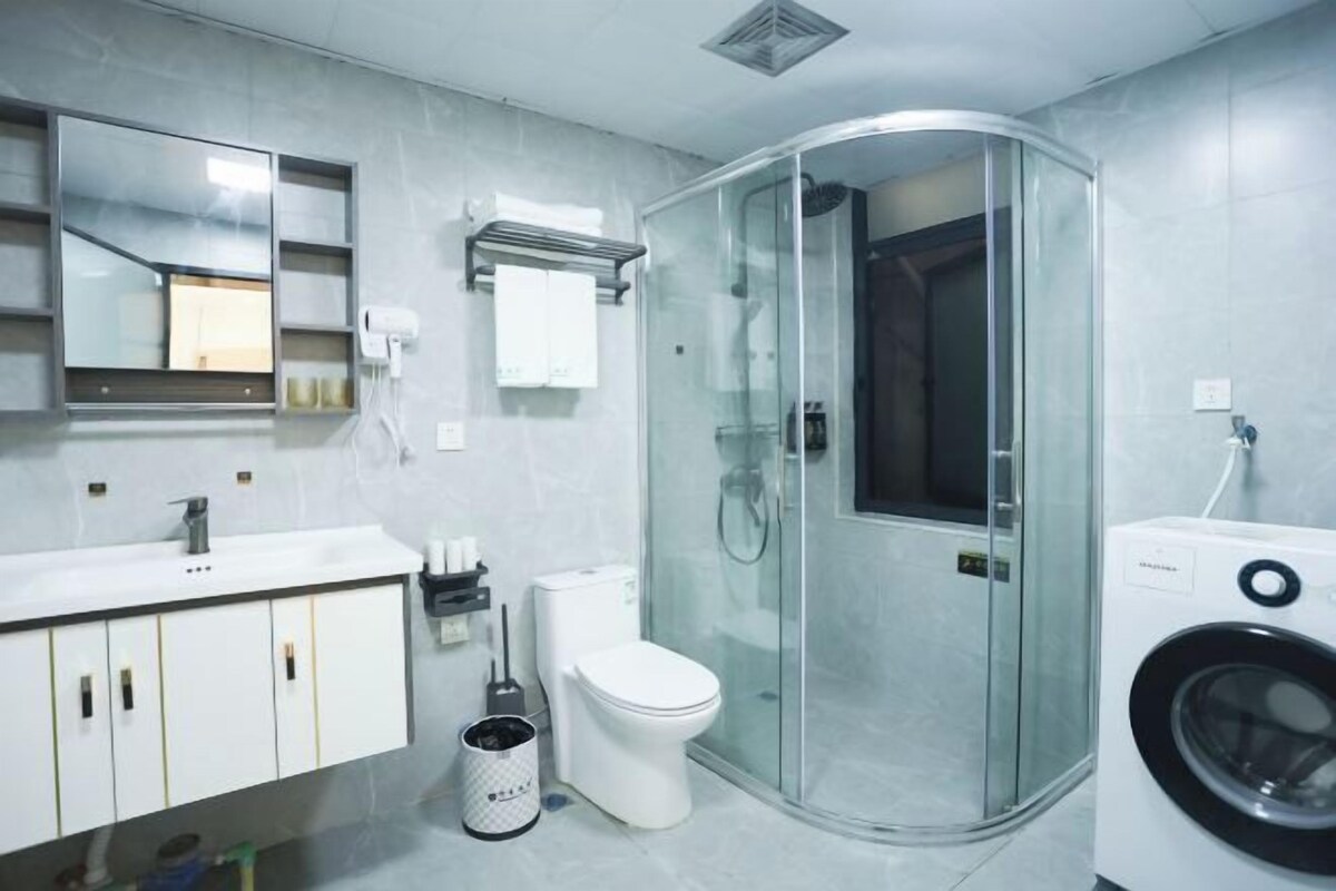 A modern bathroom with a glass shower enclosure, a toilet, a washing machine, and a sink with a mirror above it.