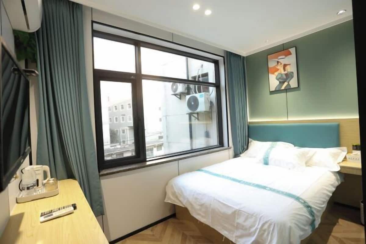 Quarto de hotel com cama, escrivaninha com cafeteira, janela com cortinas e ar condicionado.