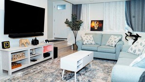 Ein modernes Wohnzimmer mit Flachbildfernseher, einer Couch, einem Couchtisch und einer Zimmerpflanze.