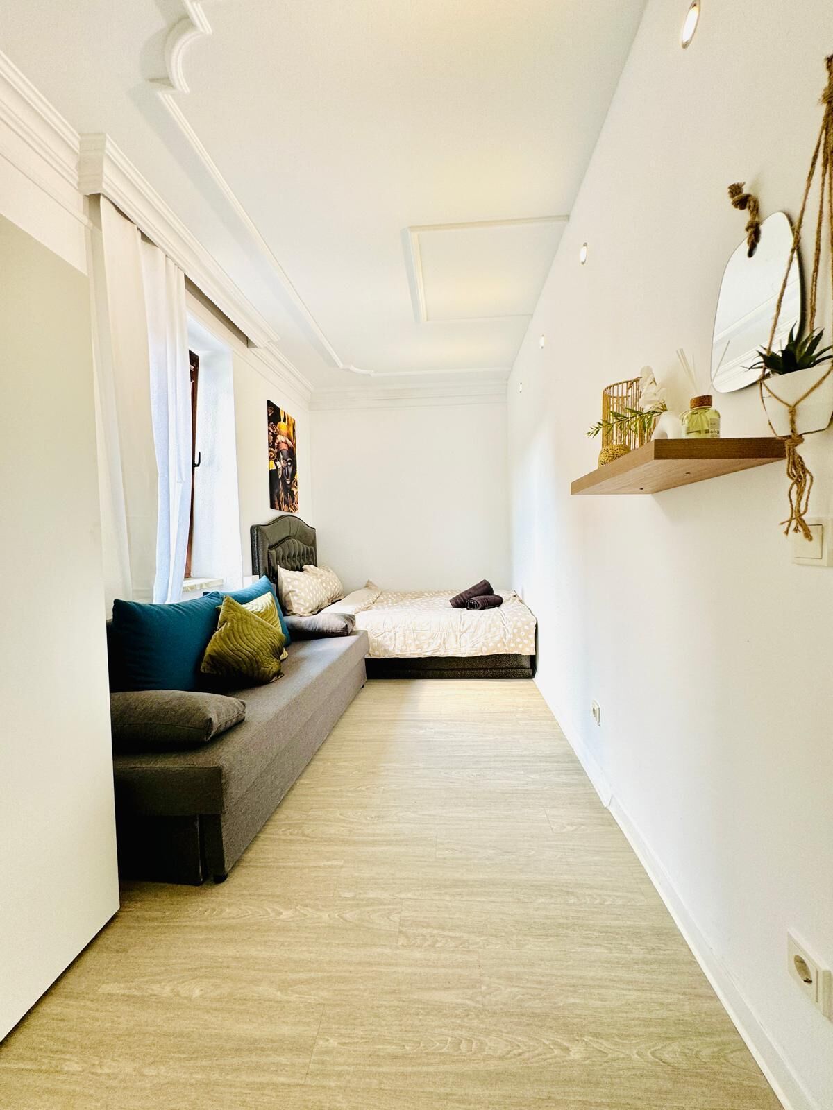 A modern, compact bedroom with a sofa bed, a small bedside table, and a wall-mounted shelf with decorative items.