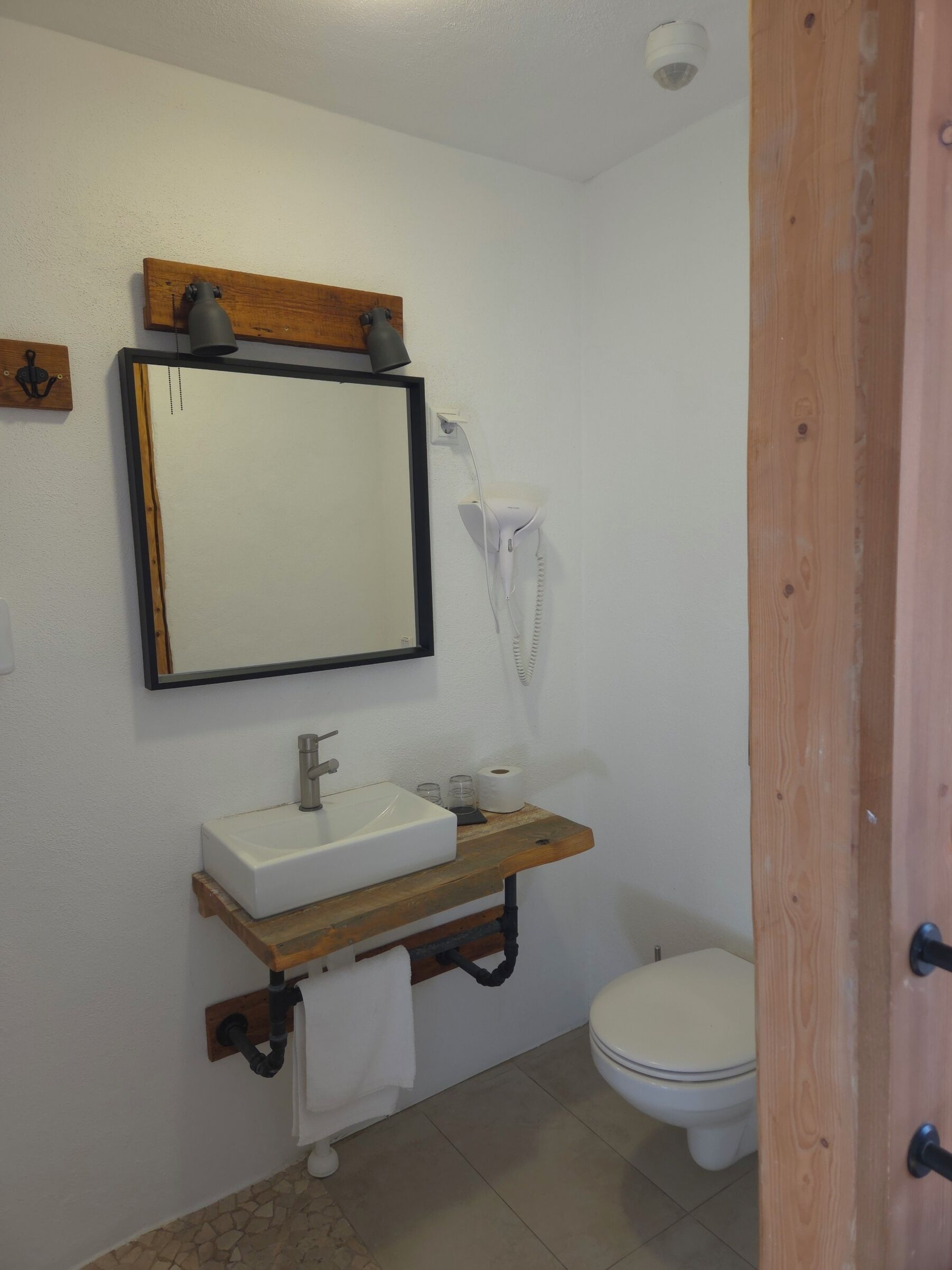 A bathroom with a white sink, mirror, and toilet. There is a towel rack and a hairdryer on the wall.
