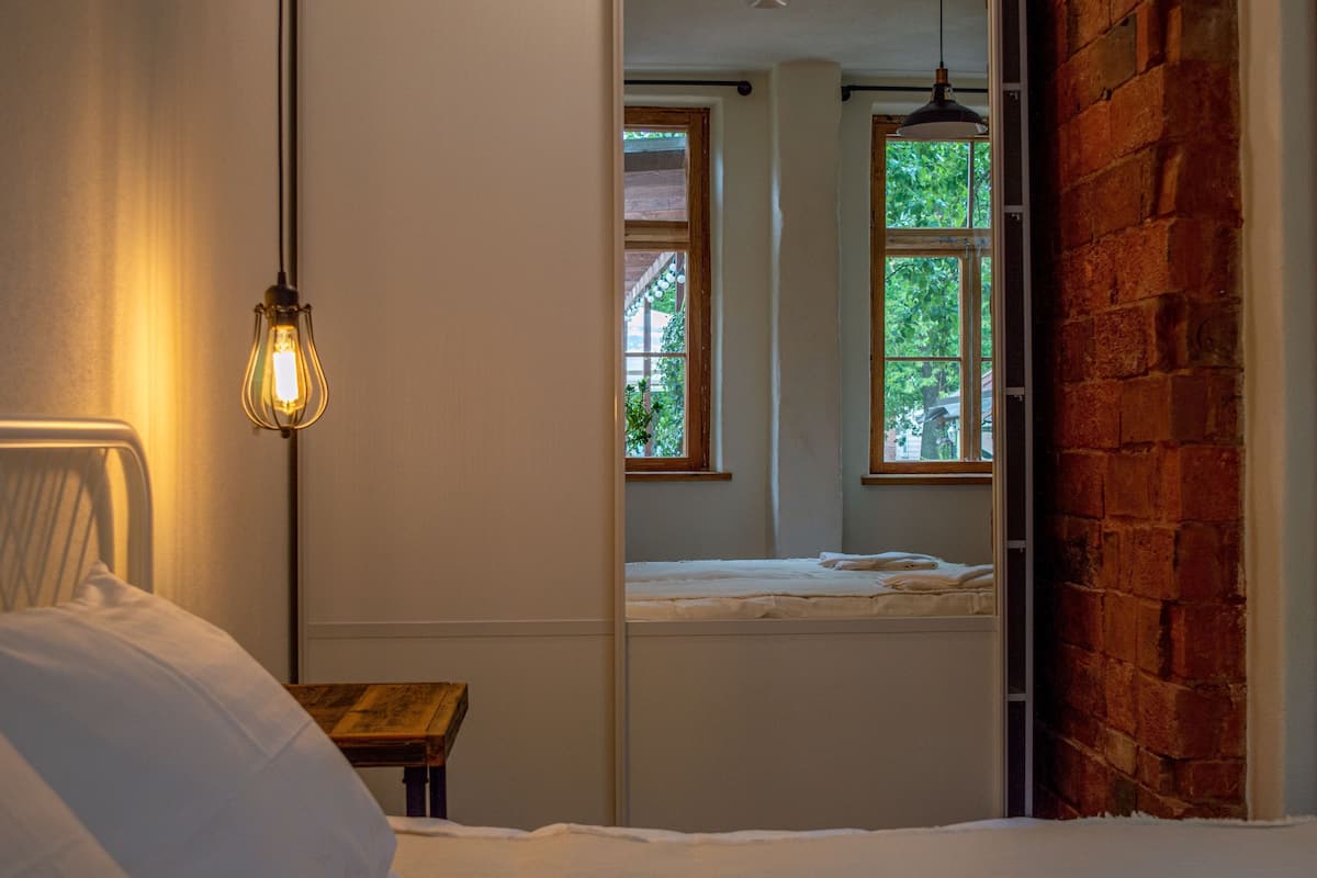 A bedroom with a bed, a hanging light fixture, a window, and a brick wall.