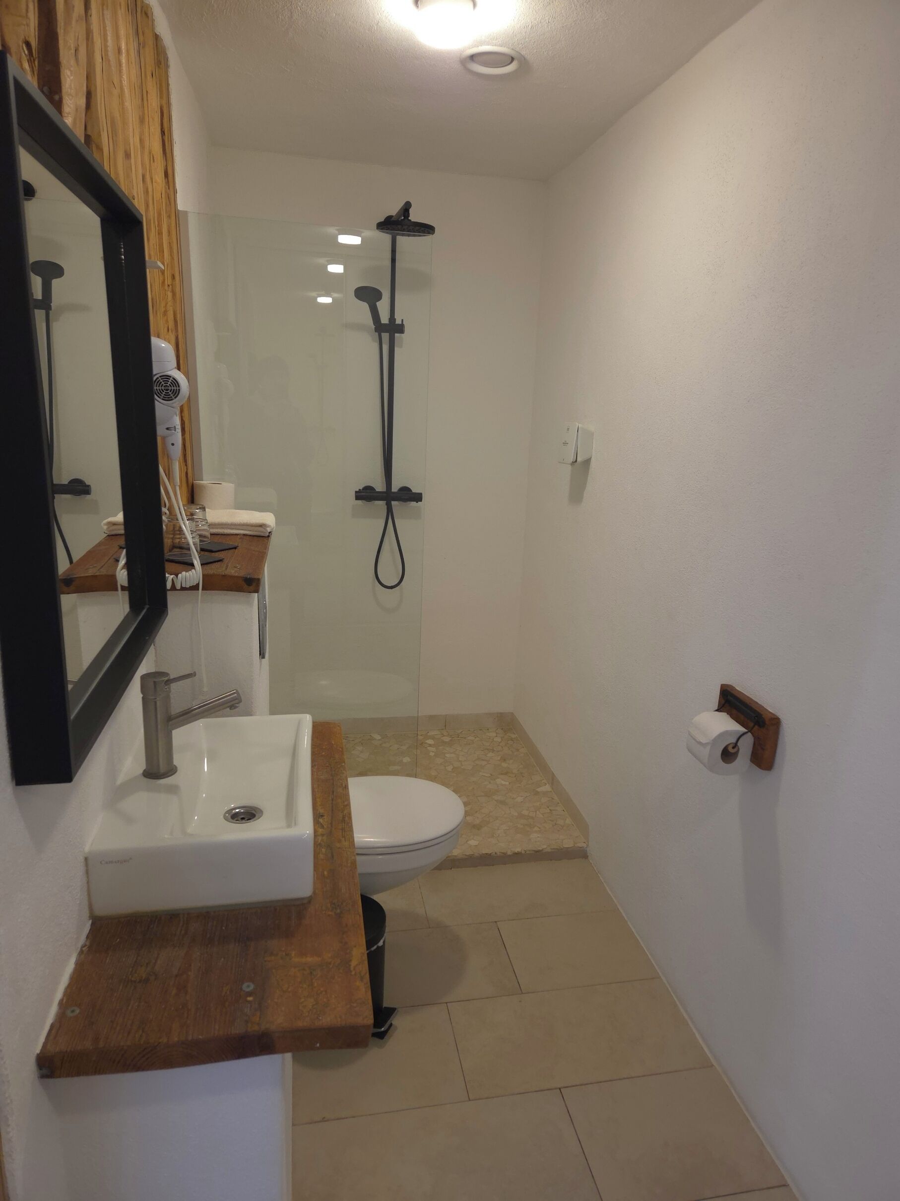 Une salle de bain avec un lavabo blanc, un miroir, une douche et des toilettes.